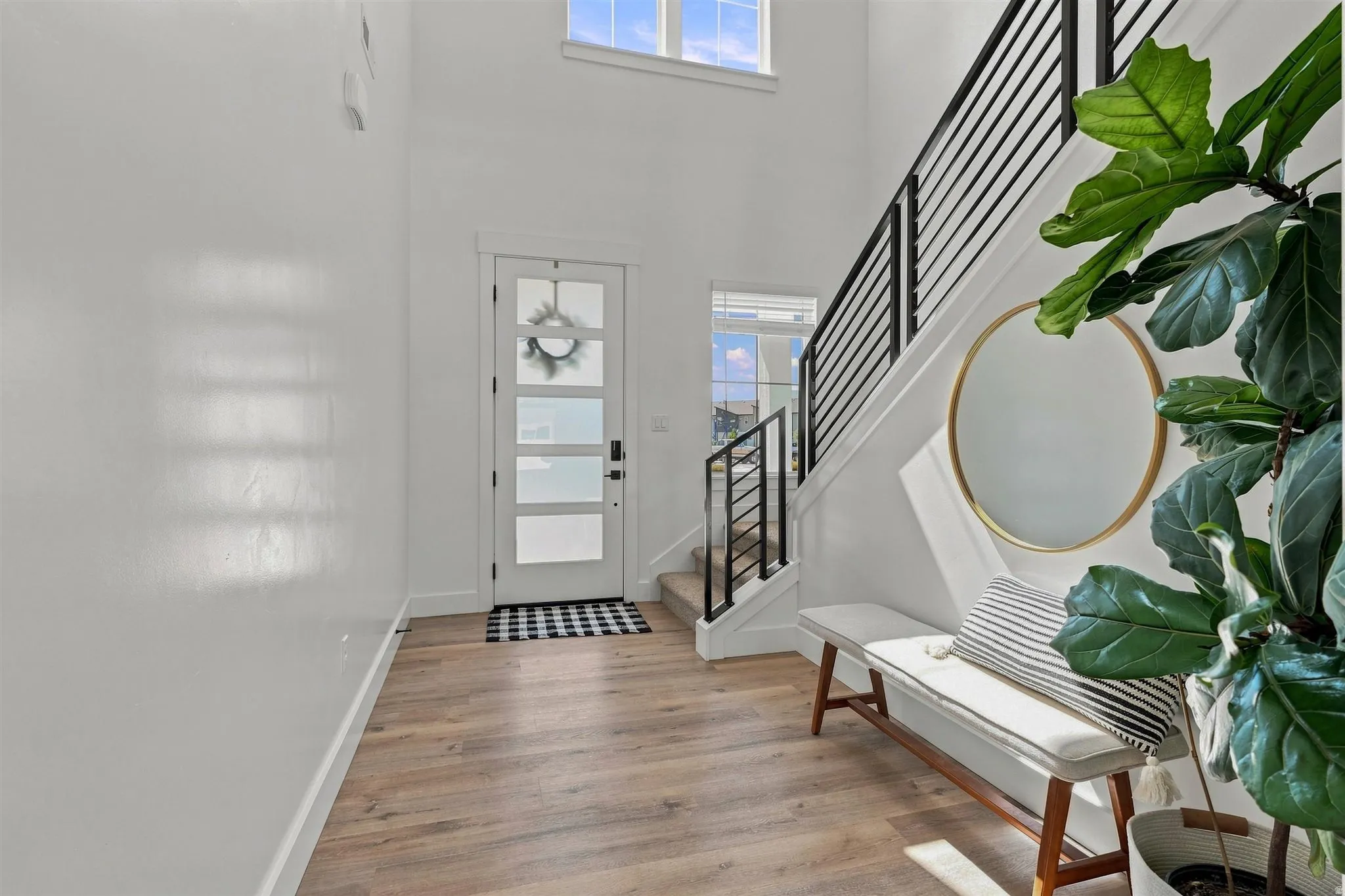 Two-story entryway with a transom window, wood-finish flooring, and a modern black metal staircase railing