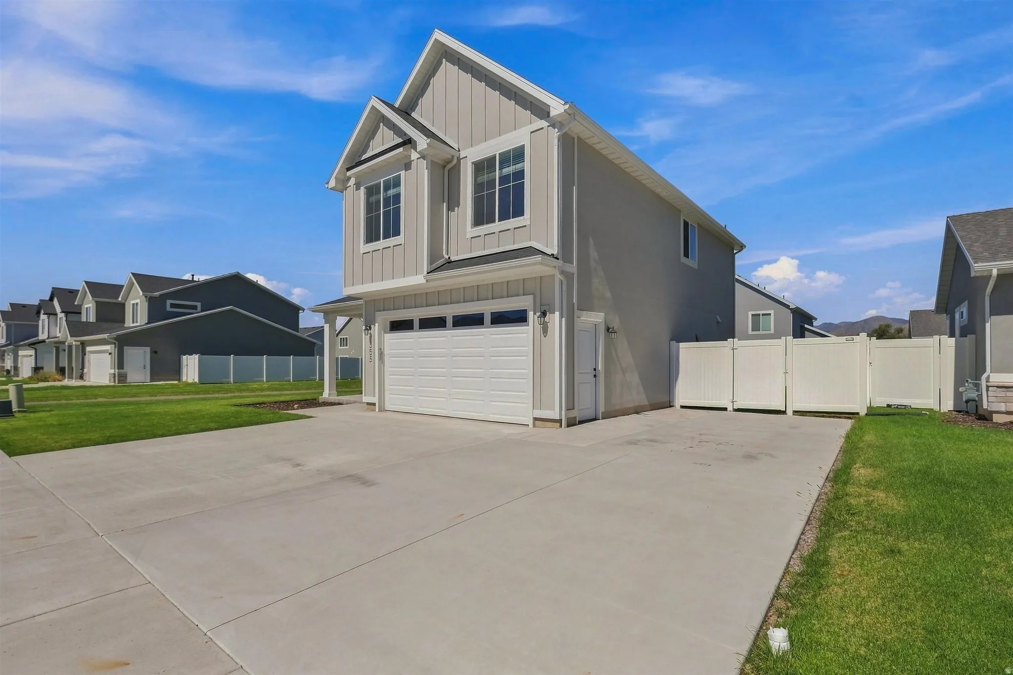 Two-story residence featuring light gray siding, white trim, a two-car garage, and a concrete driveway