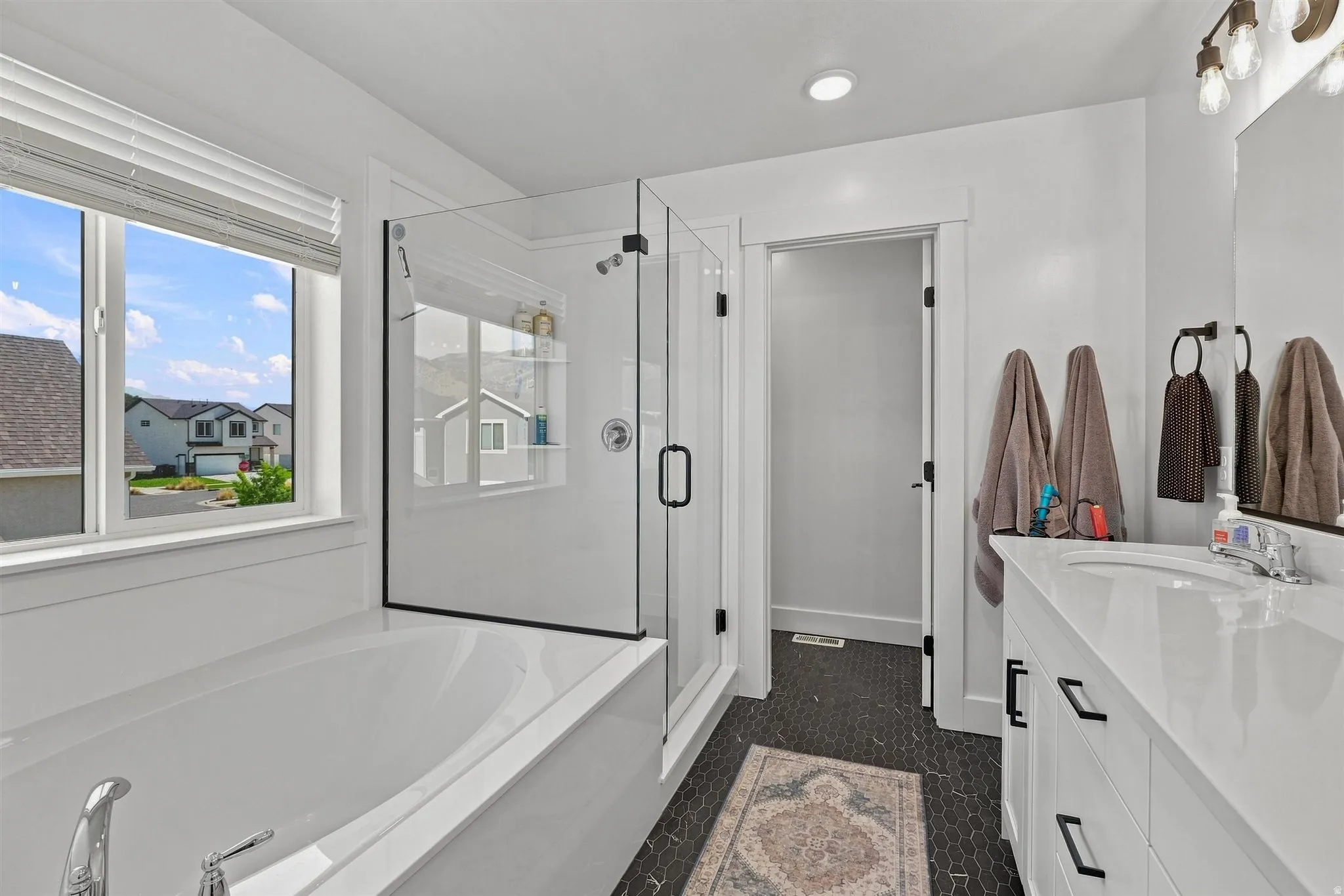 Freestanding soaking tub with polished chrome fixtures, glass-enclosed shower with matte black trim, and a white vanity with integrated sink and matte black hardware
