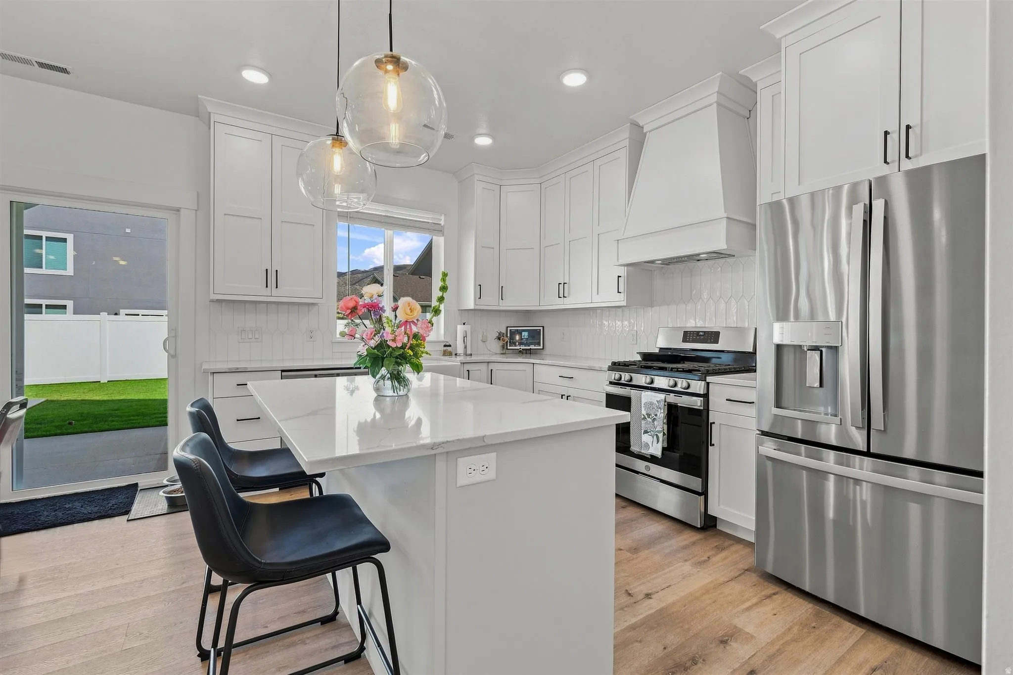 White shaker cabinetry, stainless steel appliances, central island with seating, pendant lighting, and wood-finish flooring