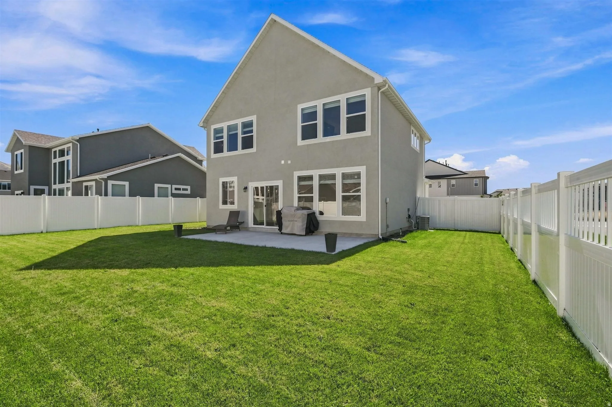 Expansive rear yard featuring a manicured lawn, concrete patio, and white privacy fencing