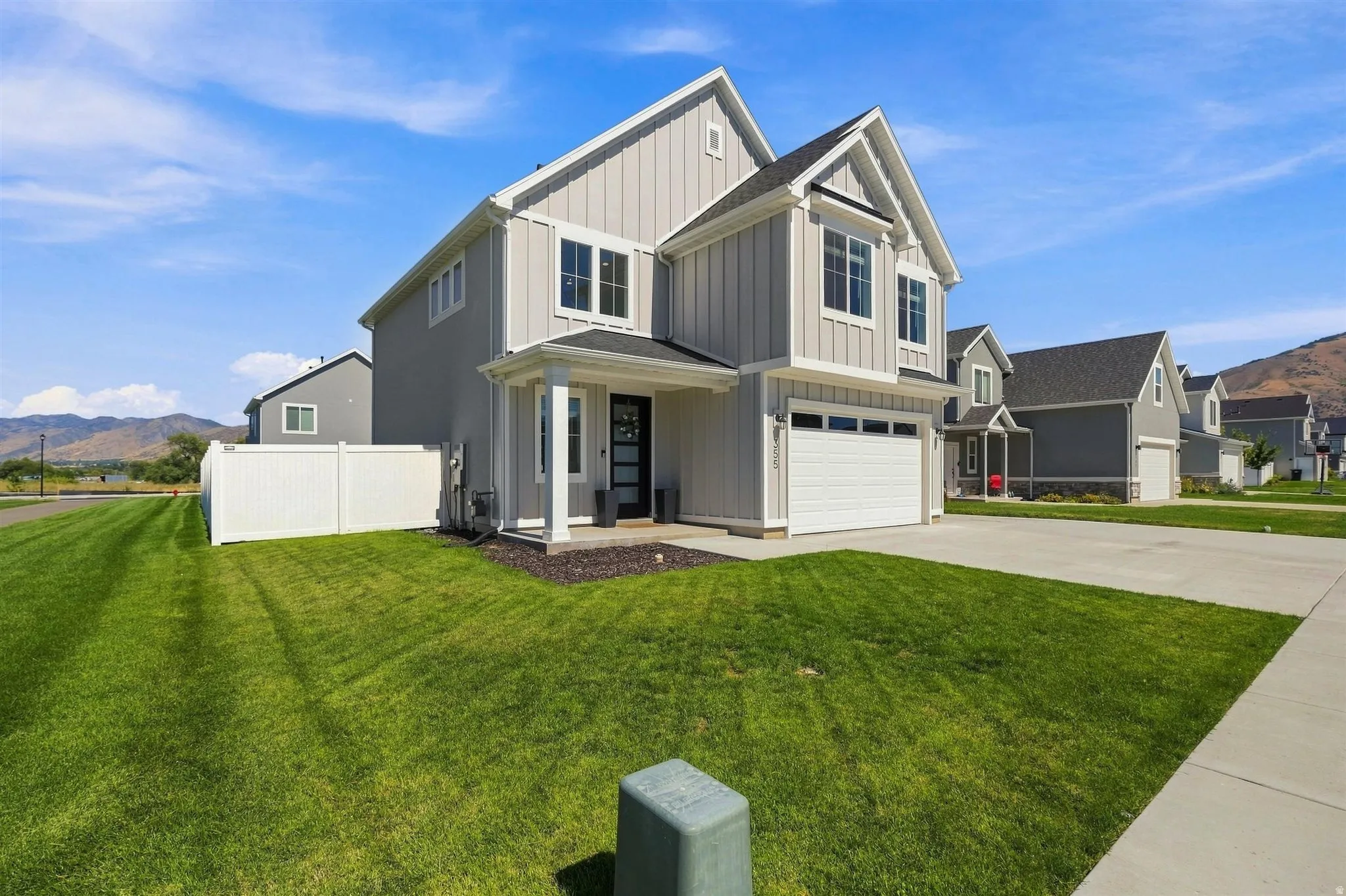 Modern two-story residence with vertical and horizontal siding, an attached garage, a covered front porch, a privacy fence, and a concrete driveway