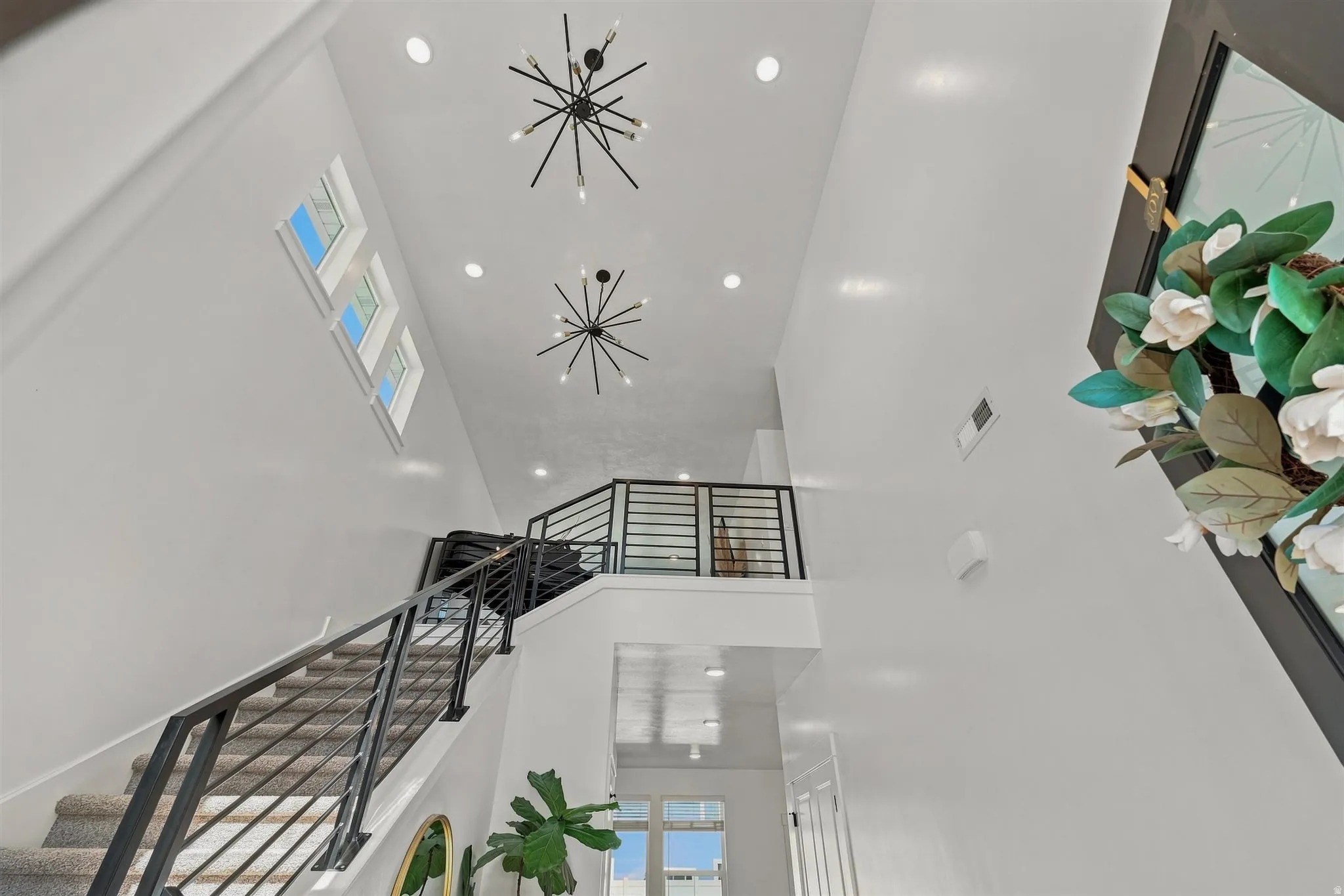 Vaulted ceiling with recessed lighting, two modern chandeliers, and a staircase featuring metal railings