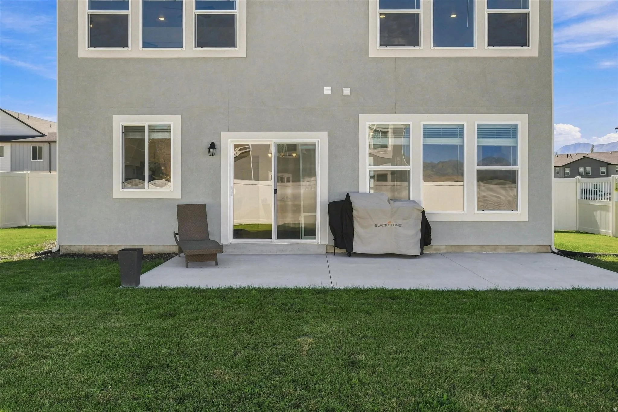 Two-story stucco exterior featuring multiple windows with white trim, a sliding glass door, an outdoor light fixture, and a concrete patio