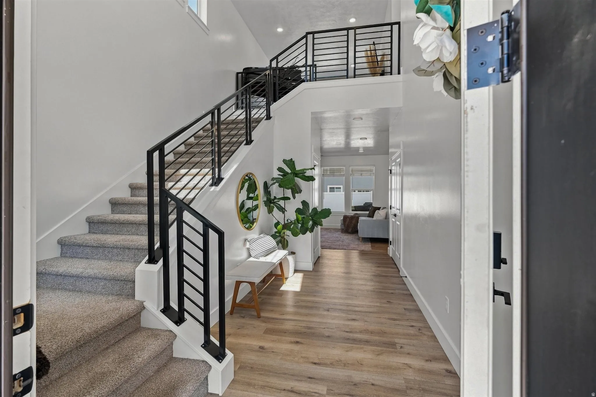 Two-story entry with wood-finish flooring, carpeted staircase, black metal railing, and high ceilings
