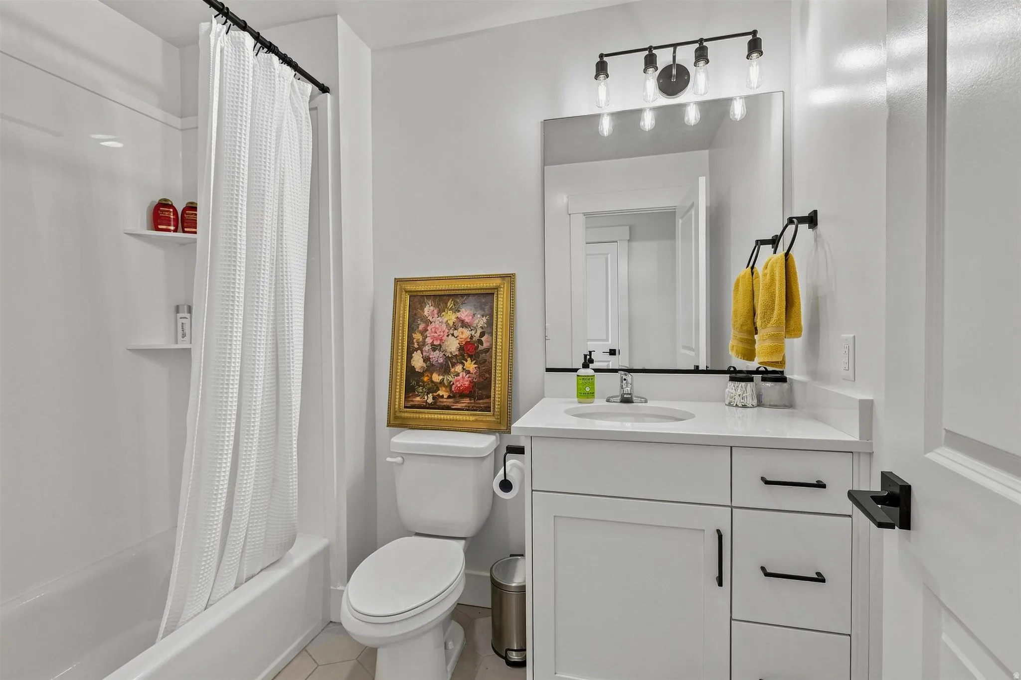 White vanity with a quartz countertop, integrated sink, and black hardware