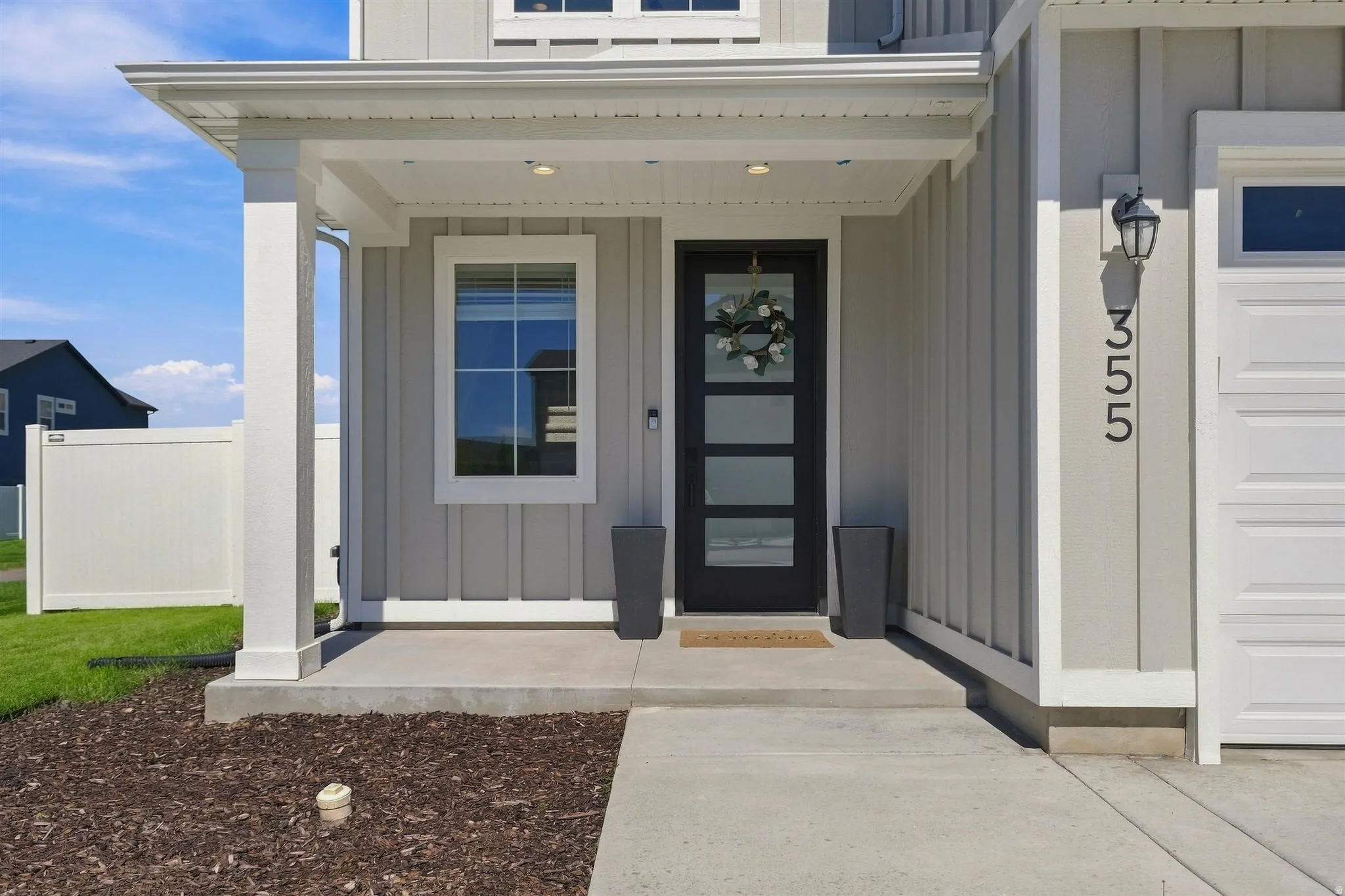 Covered entry with board and batten siding, white-trimmed window, black door with frosted glass panels, and exterior light fixture