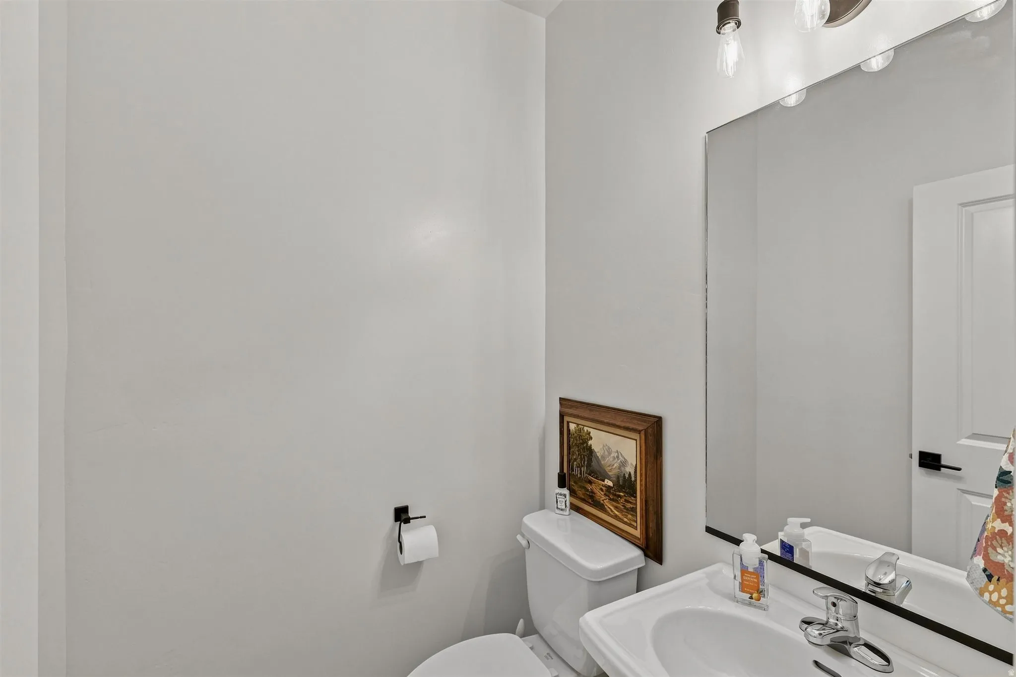 Pedestal sink with chrome faucet, large wall mirror, and modern vanity lighting