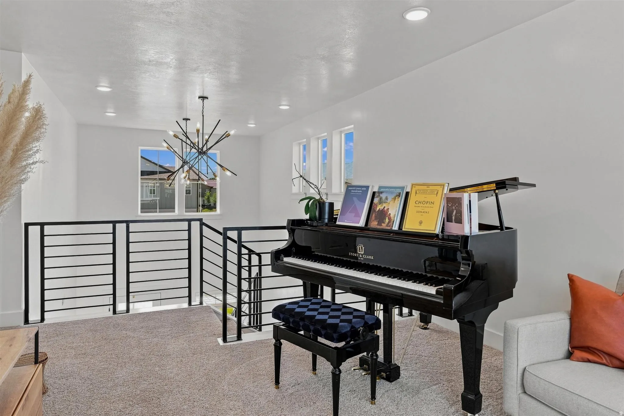 Modern chandelier fixture, recessed lighting, white walls, black horizontal bar railing, and carpeted flooring