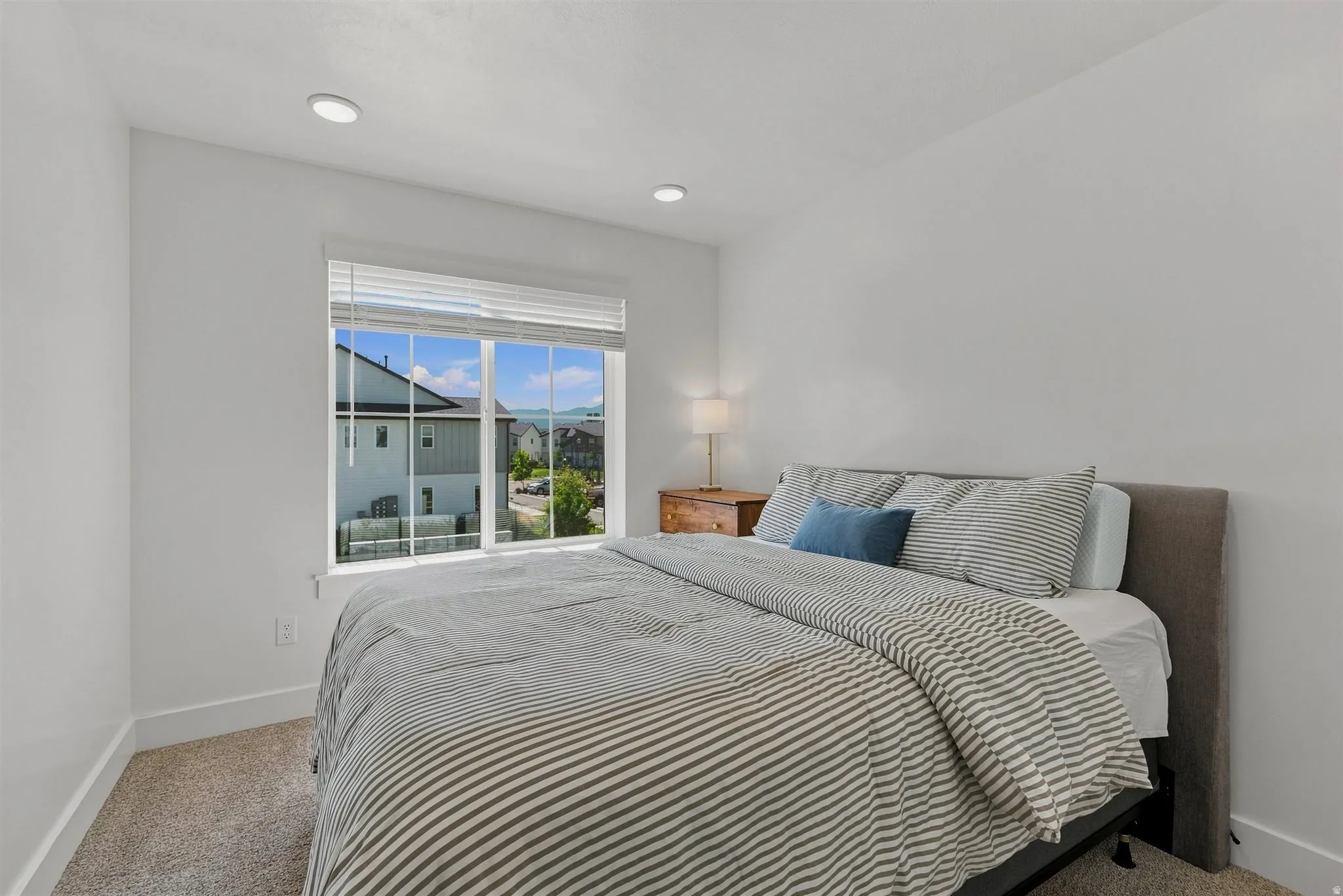 Recessed lighting, large window with blinds, and neutral carpeting