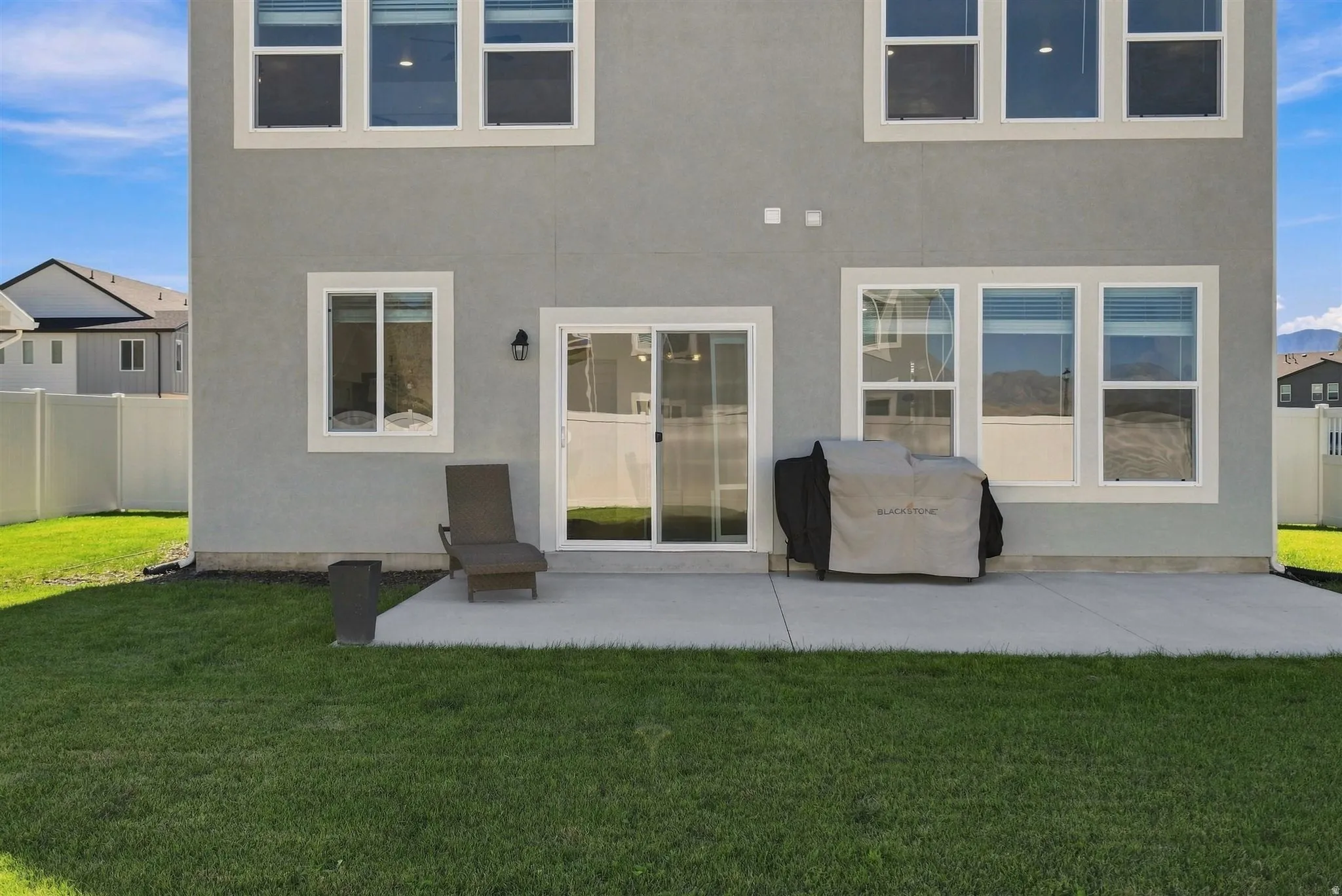 Expansive backyard featuring a concrete patio, sliding glass door, and multiple windows with white trim