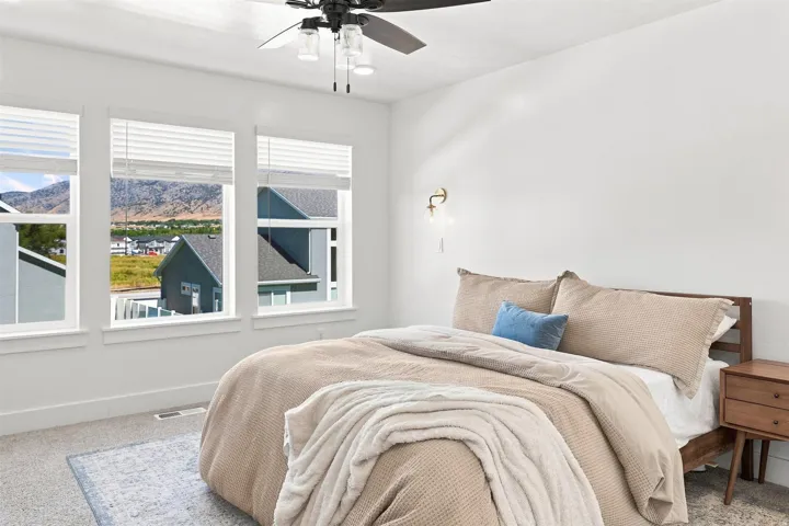 Triple windows with blinds, wall-mounted sconce, ceiling fan with integrated lighting, and carpeted flooring