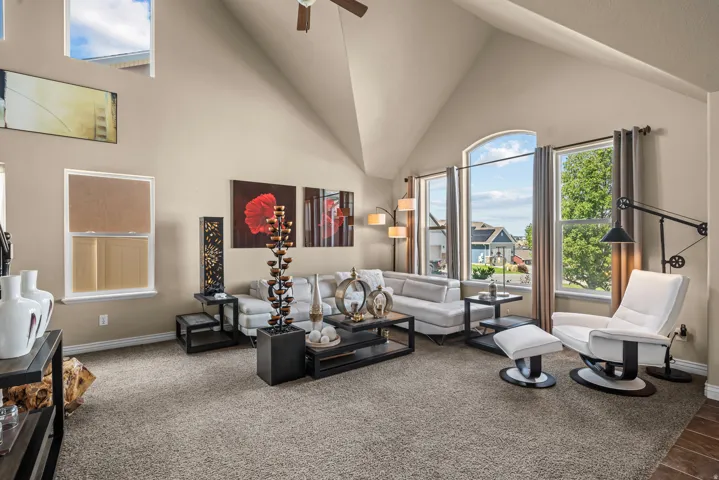 Vaulted ceiling with a ceiling fan, arched windows, light tan wall paint, and gray carpet flooring