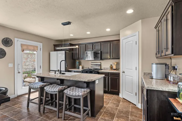 Kitchen featuring dark wood cabinetry, light-colored countertops, a central island with integrated sink, stainless steel appliances, and recessed lighting