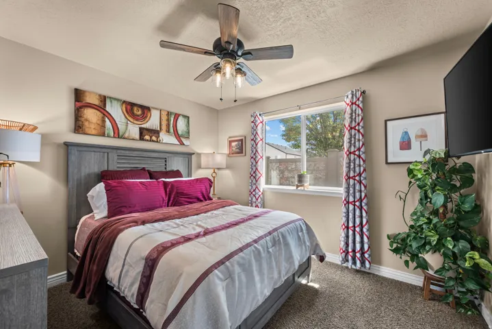 Carpeted flooring, a window with curtains, a ceiling fan with integrated lighting, and a wood-finish bed frame with an integrated headboard