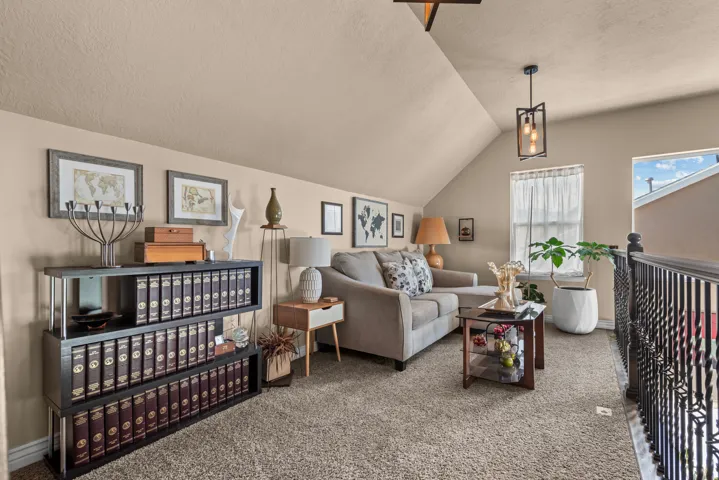 Carpeted loft area featuring a sloped ceiling, built-in shelving, decorative window, and a hanging light fixture