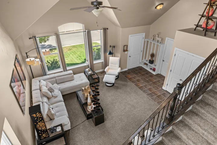 Two-story living area featuring vaulted ceilings, a ceiling fan, and multiple windows