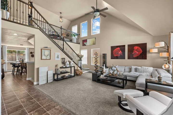 Vaulted ceiling with a ceiling fan, wrought iron staircase with a second-story landing, multiple high transom windows, tiled flooring, and carpeted flooring