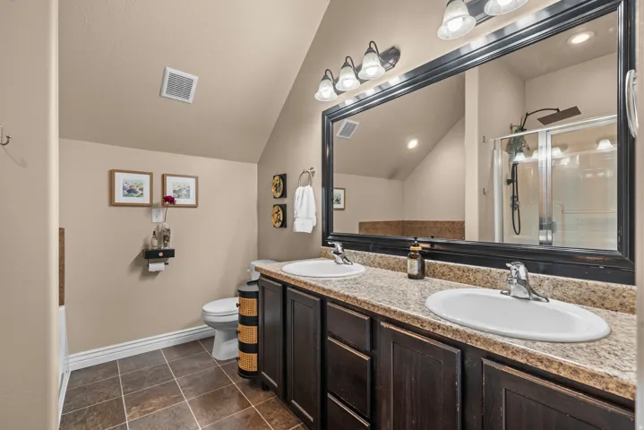 Dual undermount sinks with chrome fixtures, a spacious framed vanity mirror, dark wood-finish cabinetry, and a walk-in shower with a glass enclosure