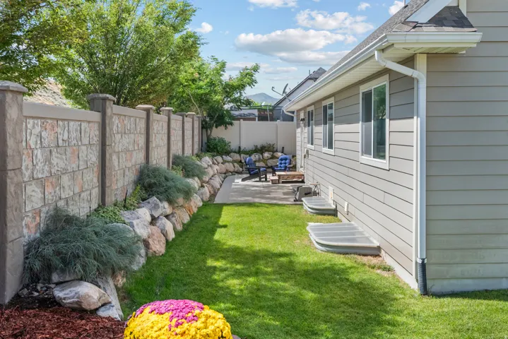 Manicured lawn with a concrete patio, stone retaining wall, and a precast concrete fence
