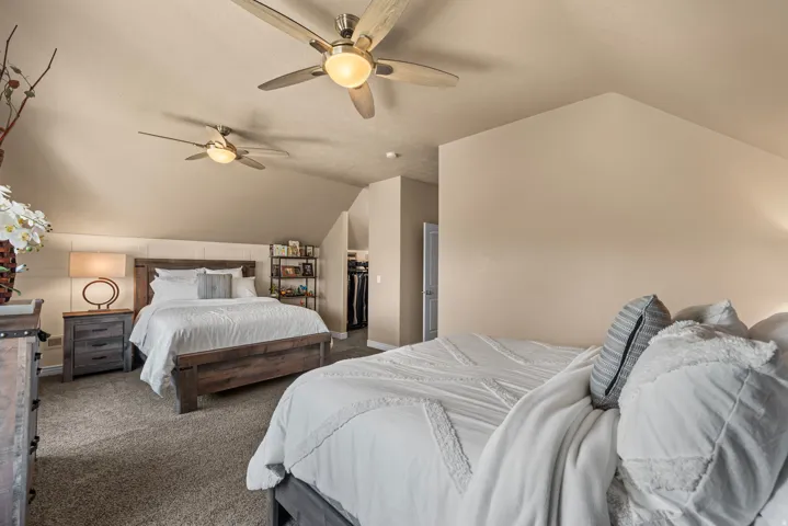 Carpeted room featuring sloped ceilings, two ceiling fans with integrated lighting, and a partial walk-in closet with built-in shelving