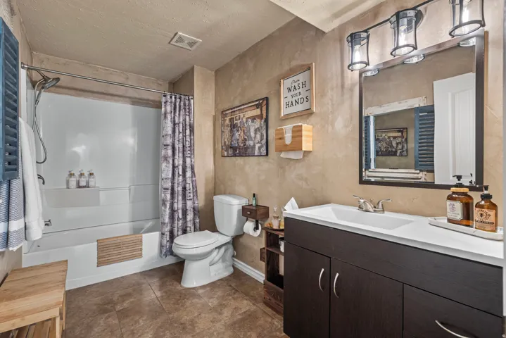 Full bathroom featuring a white tub and shower combination, dark wood-finish vanity with an integrated sink, and a framed mirror with a three-light fixture