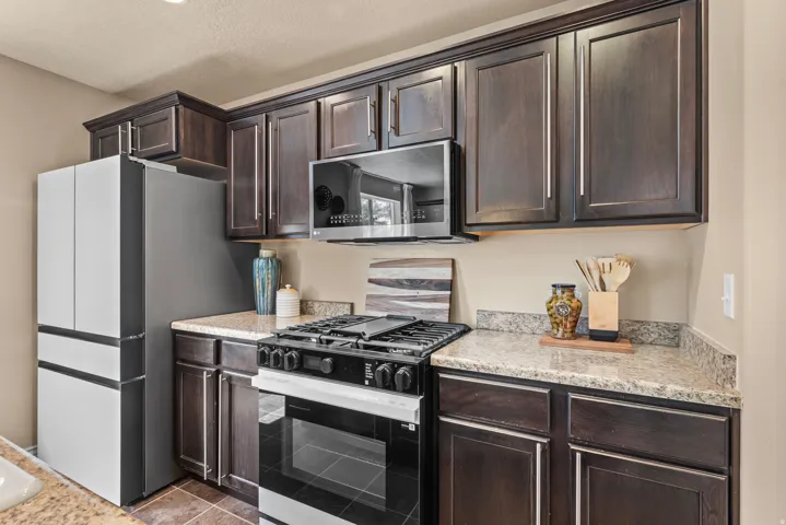 Dark wood-finish cabinetry, light-toned countertops, stainless steel appliances, and a gas range