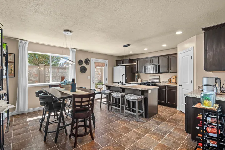 Spacious kitchen featuring dark wood cabinetry, stainless steel appliances, a center island with bar seating, and stone-finish countertops