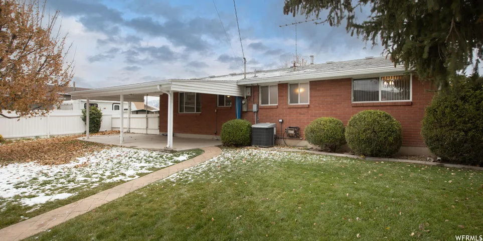 Brick exterior with multiple windows, covered carport, and a concrete patio
