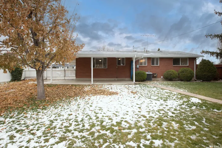 Brick exterior with white trim, covered patio, white fencing, and established landscaping