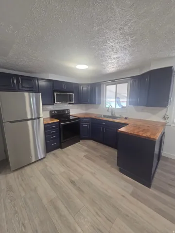 Kitchen featuring wood-finish flooring, dark cabinetry, wood countertops, stainless steel refrigerator, and integrated oven with microwave