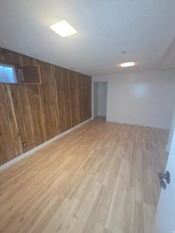 Recessed lighting, wood-finish flooring, wood panel wall, white painted wall, and a window