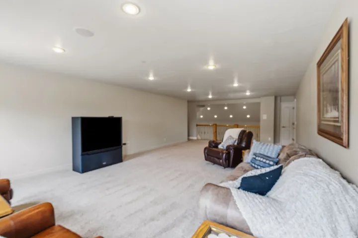 Expansive carpeted area with recessed lighting and a wood-toned railing