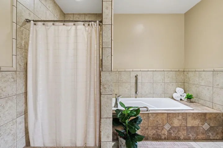 Tiled shower with a chrome curtain rod, alongside a built-in tub with a coordinating tile surround and mounted grab bar