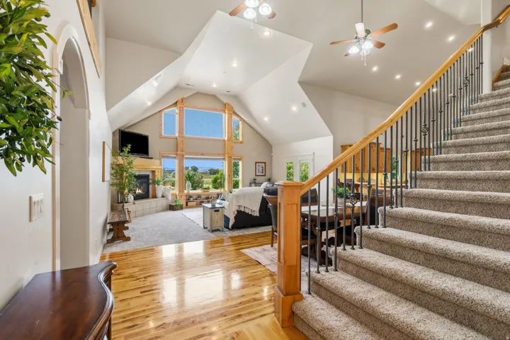 Vaulted ceiling with exposed wood beams, large picture windows, wood-finish flooring, fireplace with a tile surround, and an open staircase with wrought iron balusters