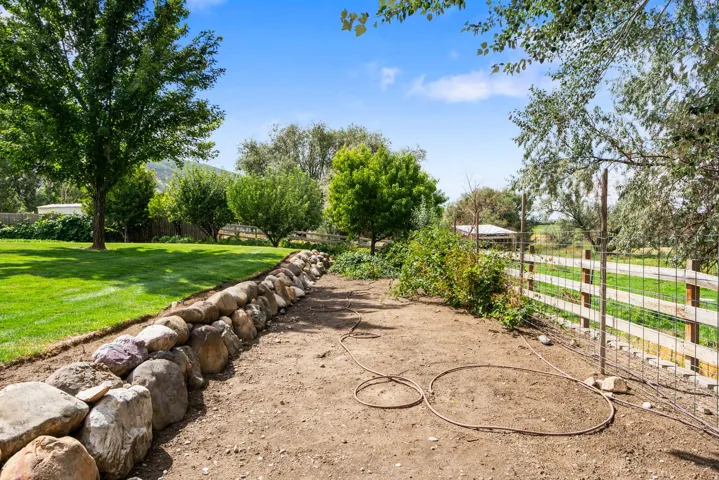 Expansive yard featuring a manicured lawn, established trees, stone retaining wall, and a wood-post fence