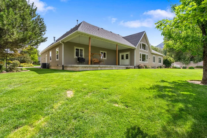 Expansive green lawn surrounding a stucco exterior with a covered patio, pitched roof, and mature trees