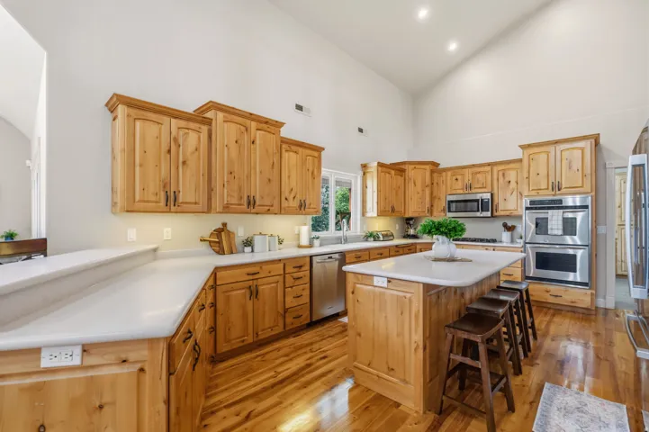 Chef's kitchen featuring custom wood cabinetry, stainless steel appliances including double wall ovens, quartz countertops, a large center island with seating, and warm wood-finish flooring throughout the open layout