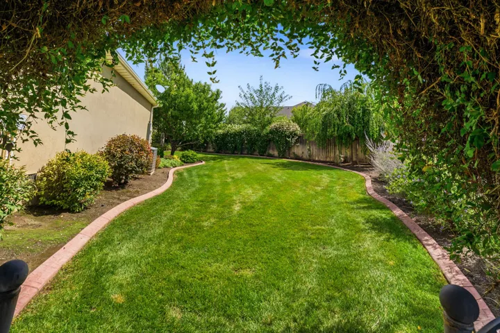 Expansive manicured lawn featuring decorative landscaping, a privacy fence, and mature trees