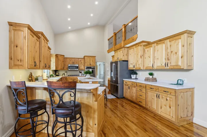 Vaulted ceiling kitchen featuring wood-finish cabinetry, stainless steel appliances, a breakfast bar, and wood-finish flooring