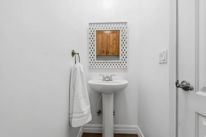 Pedestal sink with chrome fixtures, wood-finish flooring, and a mirrored medicine cabinet with wood paneling