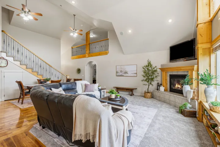 Vaulted ceilings with recessed lighting, a fireplace with a wood mantel and tile surround, wood-finish flooring, a carpeted living area, and a wrought iron staircase with wood railing