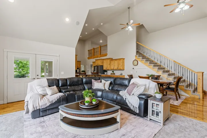 Vaulted ceilings with recessed lighting, wood-finish flooring, a staircase with wrought iron balusters, wood cabinetry, and double glass-paneled doors