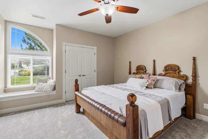 Arched window with window seat, ceiling fan, neutral wall paint, white bi-fold doors, and soft gray carpeting
