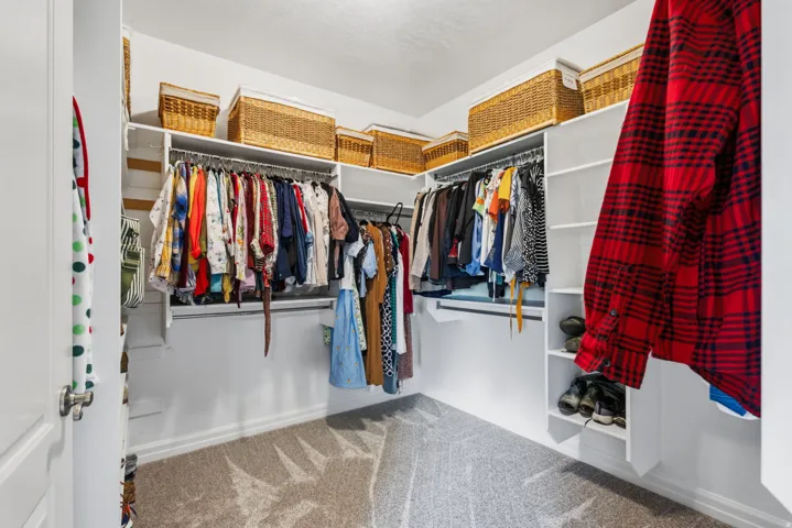 Walk-in closet featuring built-in shelving, multiple hanging rods, and patterned carpeting