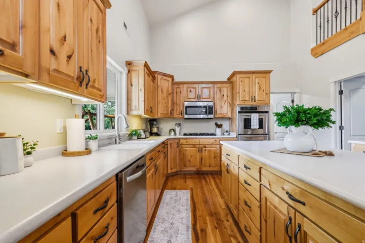 Vaulted ceiling kitchen featuring wood cabinetry, stainless steel appliances, white countertops, a large island, and wood-finish flooring