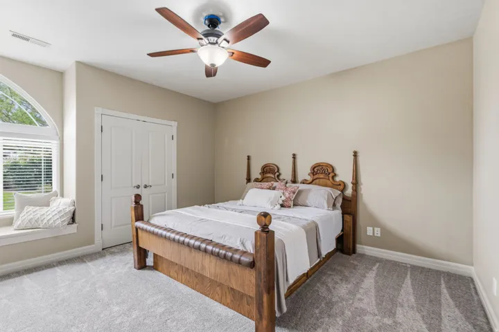 Arched window with integrated window seat, wood-finish ceiling fan, neutral wall tones, and plush carpeting