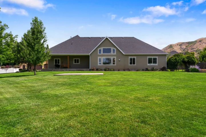 Expansive green lawn, stucco exterior, multiple windows, covered porch, concrete patio area