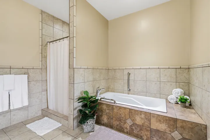 Tile-surround soaking tub with grab bars, a separate tiled shower stall, and a neutral wall color