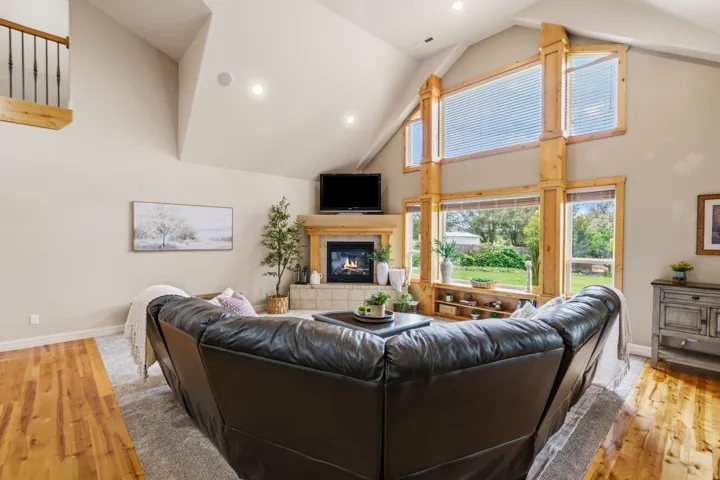 Vaulted ceiling, stone surround fireplace, natural wood-finish window frames, recessed lighting, and wood-finish flooring